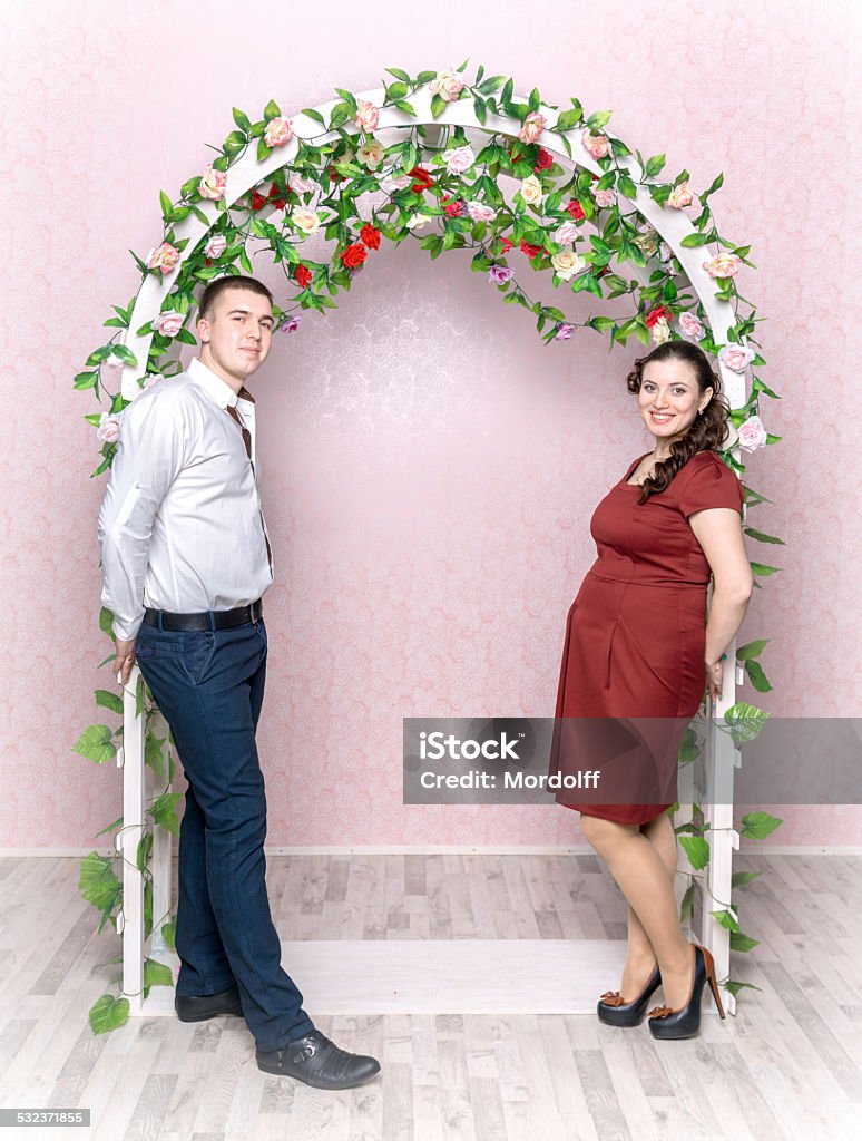 Romantic expectant parents Beautiful young couple expecting a baby standing together in the arch decorated with roses Arch - Architectural Feature Stock Photo