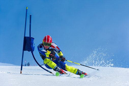 Front view of young male skier at giant slalom practice against the blue sky; pushing the blue gate