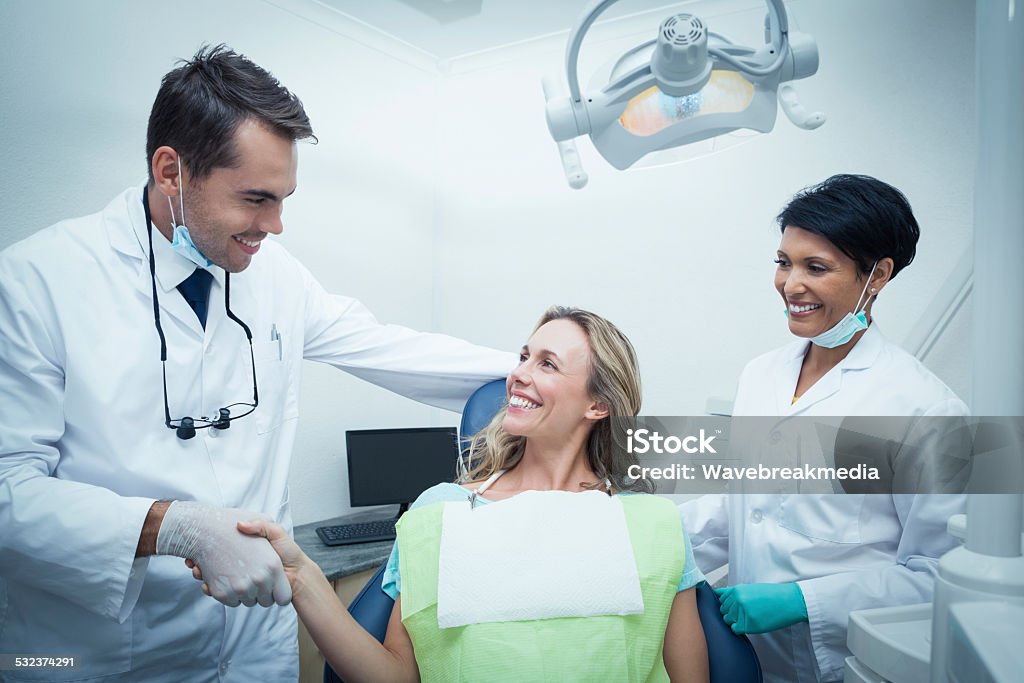 Male dentist with assistant shaking hands Male dentist with assistant shaking hands with woman in the dentists chair Dentist Stock Photo