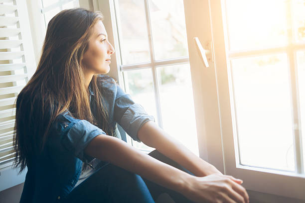 Young woman sitting and looking through window Smiling young woman sitting and looking through the window. With long hair, wears denim shirt. Hands on legs. handle photos stock pictures, royalty-free photos & images
