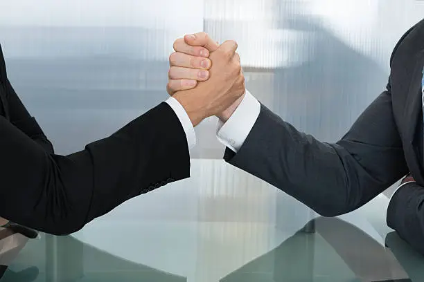 Two Businessman Holding Each Other Hands Over Desk In The Office