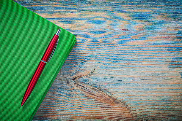 istock Closed notepad ball-point pen on wooden board top view 532388850
