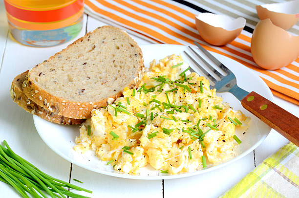 Scrambled eggs with wholemeal bread and fresh chives on white wooden table