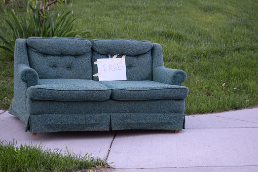 A sofa placed on the sidewalk with a sign marking it free for pick up