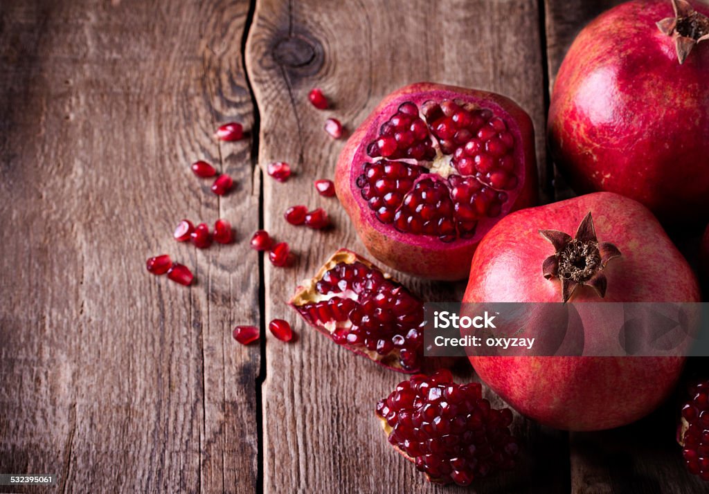 Some red pomegranates on old wooden table Some red juicy pomegranate, whole and broken, on dark rustic wooden table Pomegranate Stock Photo