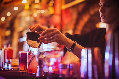 Midsection of a young female bartender preparing a cocktails in a nightlife cocktail bar. Selective focus. Focus on foreground.