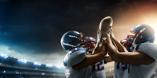 Football Players celebrate their victory Group of tough American football players celebrating their victory. They are holding the ball all-together. The action takes place on professional stadium. Players wear unbranded sports uniform. football team stock pictures, royalty-free photos & images