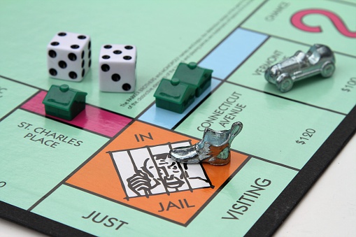 West Palm Beach, USA - August 15, 2013: A partial view of the Monopoly game board showing the Jail space. The Shoe game piece is in jail and the Race Car game piece is two spaces away. Dice and several houses  are also placed near the Jail space. Monopoly is a strategy game owned and manufactured by Hasbro.