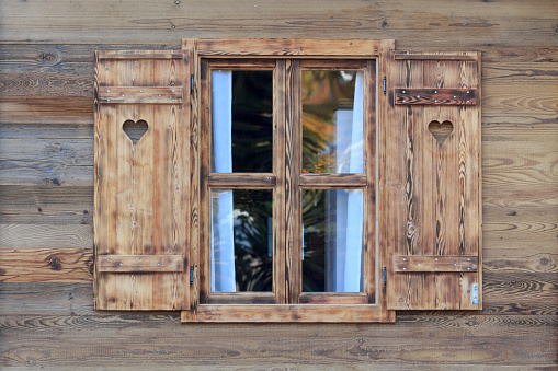 Stock photo showing close-up view of colourful orange house exterior in Burano, Venice, Italy with two wood framed casement windows with wooden shutters and Venetian blinds. Famous for lace making, Burano is an island in the Venetian Lagoon.