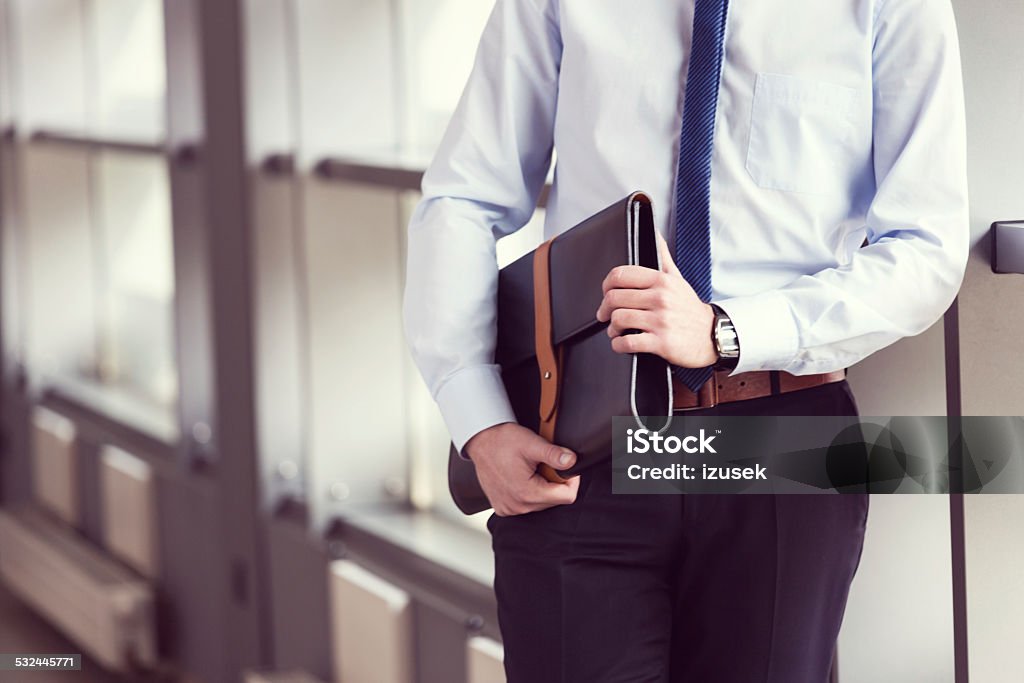 Businessman holding briefcase, close up Businessman standing in a meeting room, wearing shirt and tie, holding leather briefcase. Close up of hands. Briefcase Stock Photo