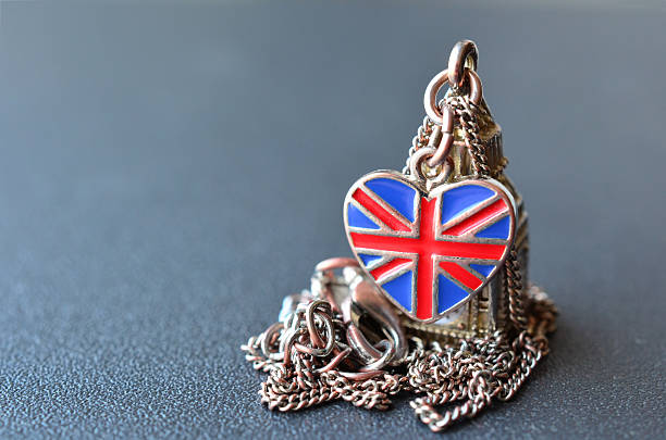 UK souvenir Souvenir from Great Britain - necklace with pendant of Big Ben figure and heart shaped British flag on gray metal surface with shallow depth of field against grey and blue bokeh London Memorabilia stock pictures, royalty-free photos & images