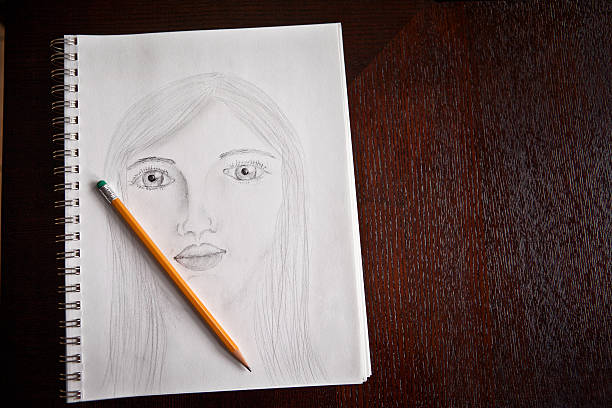 An open sketchbook with a portrait of a woman and a pencil laying on a table.  (note to inspector: drawing created by photographer)