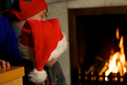 two kids with christmas hat waiting front the fireplace