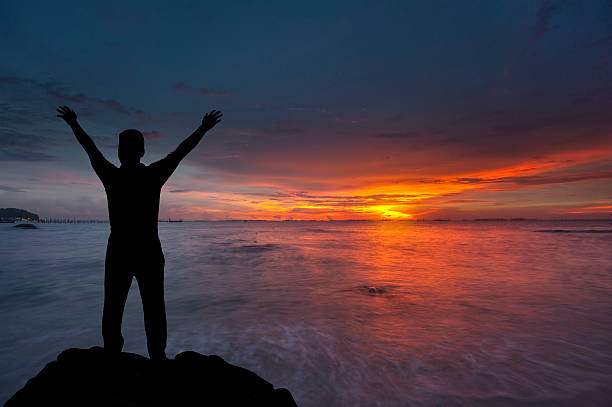 istock Silhouette of boy with hands raised to beautiful sunset 532517225