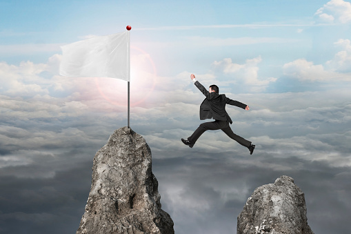 businessman jumping over mountain peak to blank flag with natural sunlight cloudscapes background