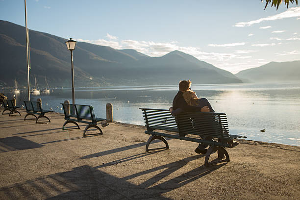 belo casal sentado no banco agarrar ao pôr do sol assistir lago - contemplation silhouette tree men imagens e fotografias de stock