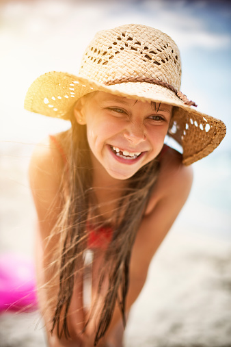 Portrait of a little girl laughing at the beach. The girl aged 8 is wearing a straw cowboy hat and has a long hair. Closeup portrait. 