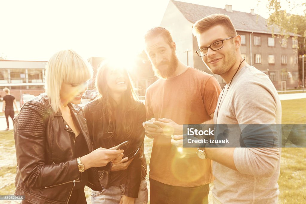 Group of friends using smart phones at sunset Outdoor portrait of group of young people using smartphones together at sunset. 2015 Stock Photo
