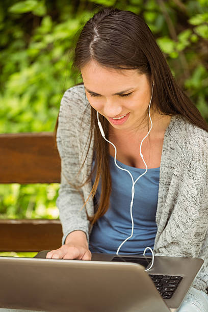 smiling student sitting on bench listening music and using laptop - school bench above bildbanksfoton och bilder