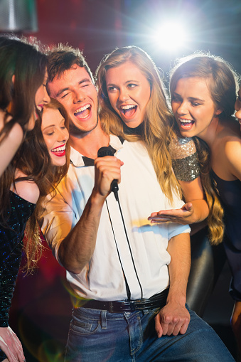 Happy friends singing karaoke together in a bar