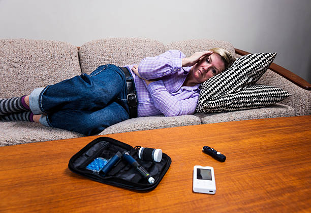 Diabetic person experiencing hypoglycaemia or a sugar crash. A middle-aged diabetic woman suffering from a glucose crash, also known as a diabetes sugar crash or hypoglycaemia lying on a couch at home.. hypoglycemia. stock pictures, royalty-free photos & images