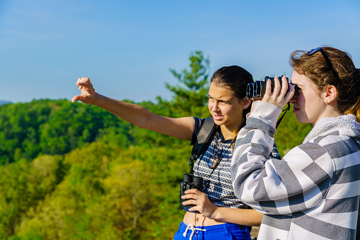 Teenager girl with binocular explore scenic view to Great Smoky Mountains and Cherokee National Forest from the Turkey Creek Overlook at Cherohala Skyway, Tennessee, North America, USA. Elevation 2630Ft.