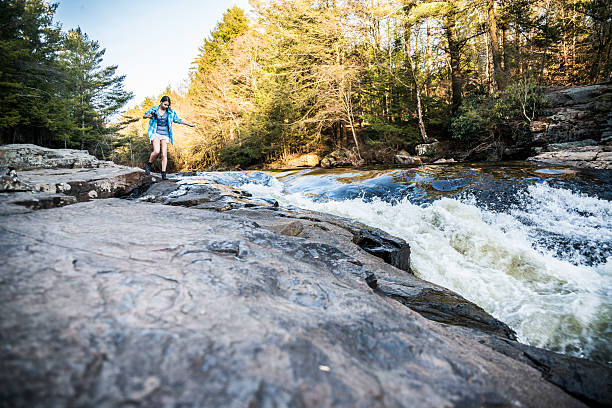 Teenager girl explore nature in Poconos, Pennsylvania Teenager girl explore the nature in the Austin T. Blakeslee Natural Area, Poconos, Pennsylvania, USA. Girl walks on the rocks  on the shore of the forest river Tobyhanna Creek, next to the Tobyhanna Falls, at early spring. the poconos stock pictures, royalty-free photos & images
