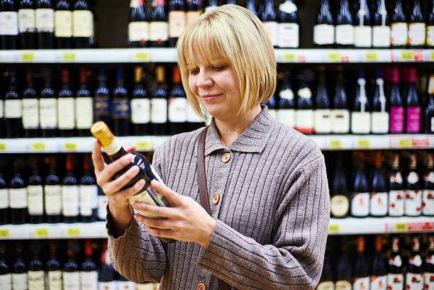 Woman reading label on bottle of wine in store