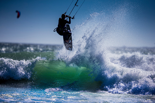 A low angle shot of a person surfing and flying a parachute at the same time in Kitesurfing. Bonaire, Caribbean