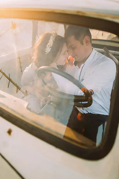 Portrait of a young girl with floral headband and handsome man sitting in a vintage car and smiling face-to-face.