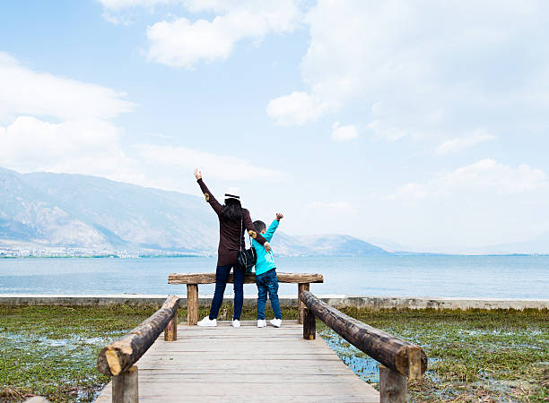 Mother and son raising hands while standing on lakeside jetty.