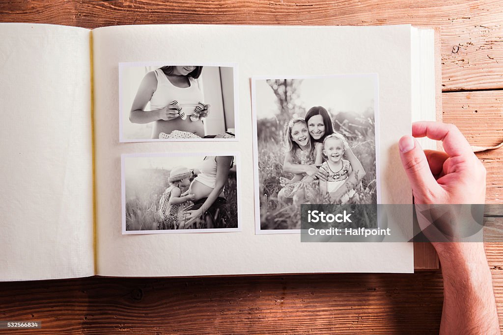 Mothers day composition. Photo album, black-and-white pictures. Mothers day composition. Hands of unrecognizable man holding a photo album, black-and-white pictures. Studio shot on wooden background. Photo Album Stock Photo