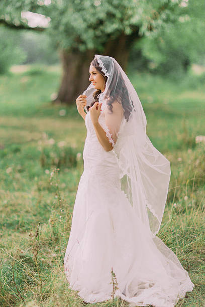 istock Beautiful bride in white dress playing with veil, spring green 532567510
