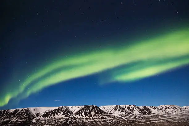 Green northern lights in Icelandic snow mountains.