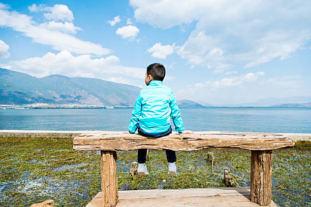 istock Little asian boy sitting on lakeside jetty 532570078