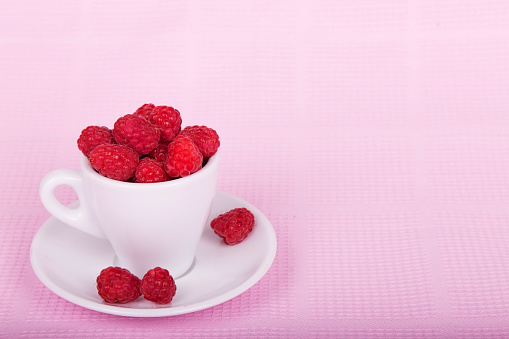 Fresh raspberries in a white cup on a pink background