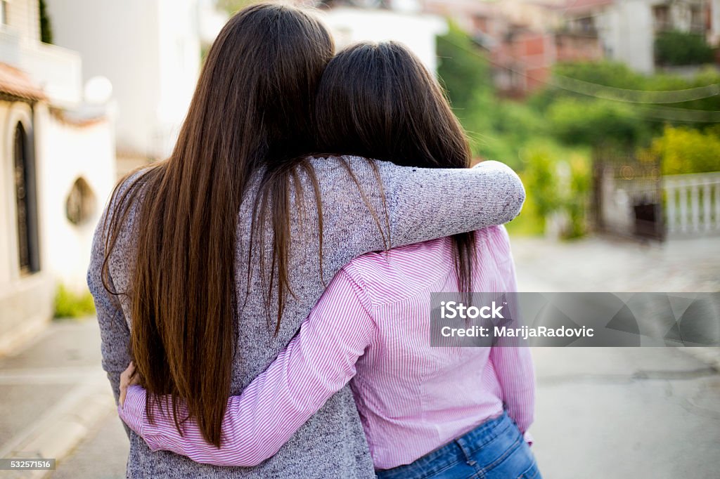 Two identical teenage girlfriends, shot from back Embracing Stock Photo