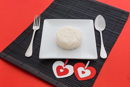 cooked rice with a spoon and fork on white dish in Platemat on red background
