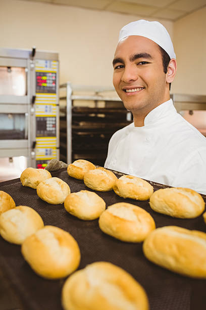istock Baker smiling at camera holding tray of rolls 532574197