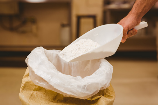 Baker scooping flour out of sack in a commercial kitchen