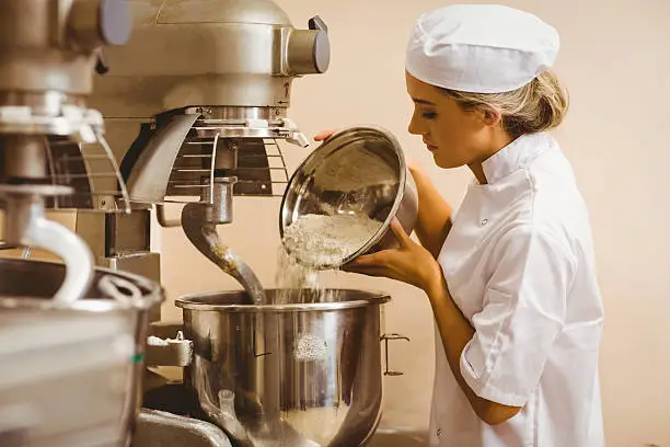 Baker pouring flour into large mixer in a commercial kitchen