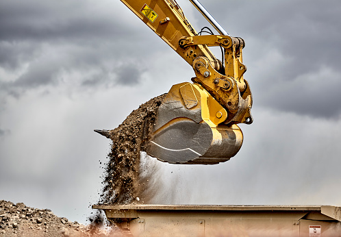 Mature construction site worker sitting in a small excavator and using smart phone at the construction site.