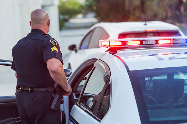 Police officer getting out of cruiser Policeman pulls over a driver for speeding, getting out of police car to write a traffic ticket. car back open stock pictures, royalty-free photos & images