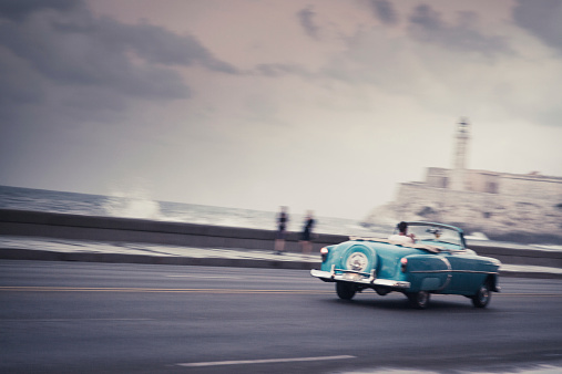 one of Havana's many classic cars drives along the city's famous seaside promenade