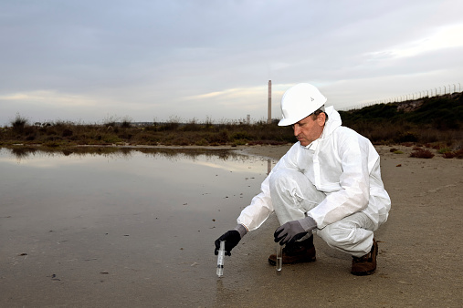 Worker in a protective suit examining pollution in the water at the industry.