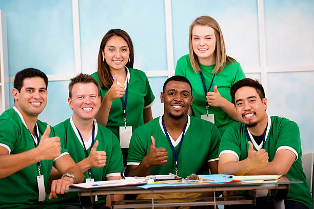 Multi-ethnic group of volunteers organize disaster relief or donation efforts.  They discuss plans during meeting and give thumbs-up.  Disaster relief, global aid, charity and relief work themes. 