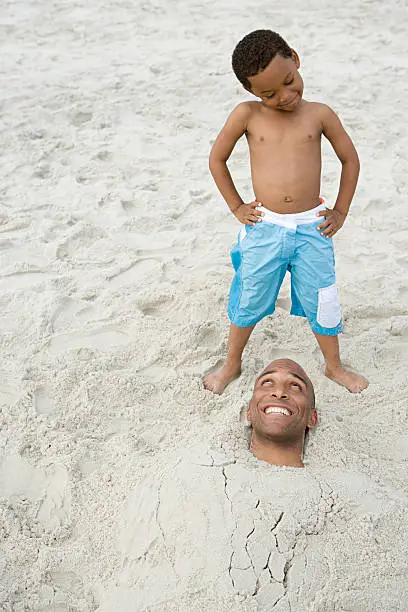 Photo of Son looking at father buried in sand