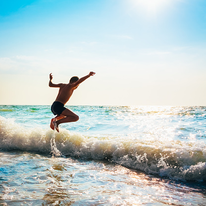 Boy Jumping In Sea Waves. Jump Accompanied By Water Splashes. Summer Sunny Day, Ocean Coast
