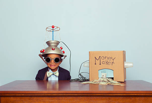 Young Business Boy wearing Mind Reading Helmet Makes Money A young boy and businessman feeds his money making machine with great ideas and out comes lots of US Dollars. Bling. Boy dressed in business suit with Benjamin Franklin bow tie. Retro styled. If making money was easy, it would be awesome. super money stock pictures, royalty-free photos & images