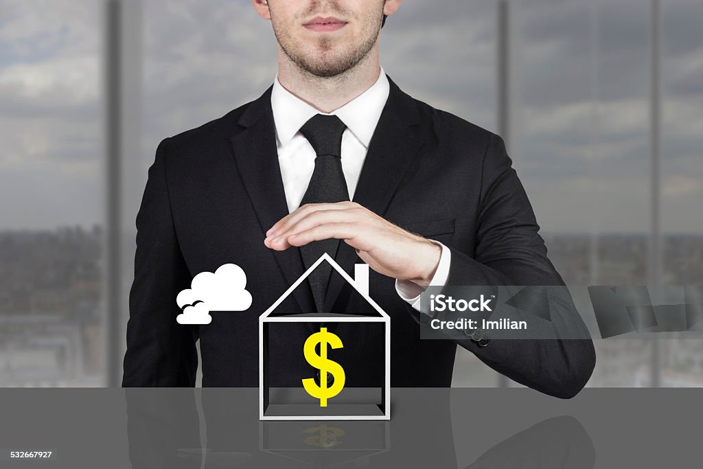 businessman holding protective hand above house dollar symbol businessman in office holding protective hand above house dollar symbol 2015 Stock Photo